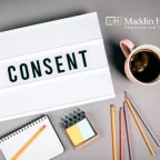 The word consent in a lightbox with pencils and a mug of coffee